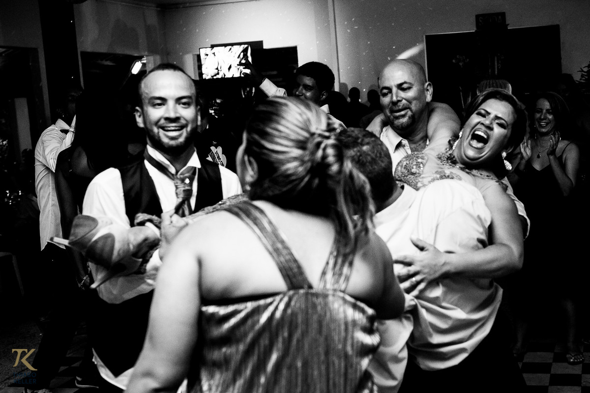Fotografia de casamento de Lívia e Paulo Henrique na cidade de Paracatu, Minas Gerais. Mãe do noivo é carregada pelos filhos na pista de dança. Foto em preto e branco.