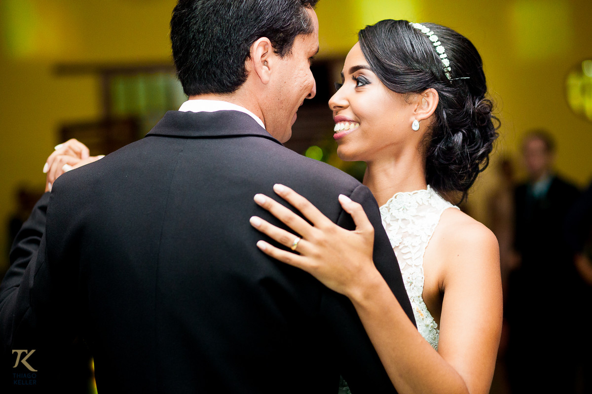 Fotografia de Casamento de Maura e Thiago realizado na cidade de Paracatu, Minas Gerais. Noiva sorri para o noivo enquanto dançam.