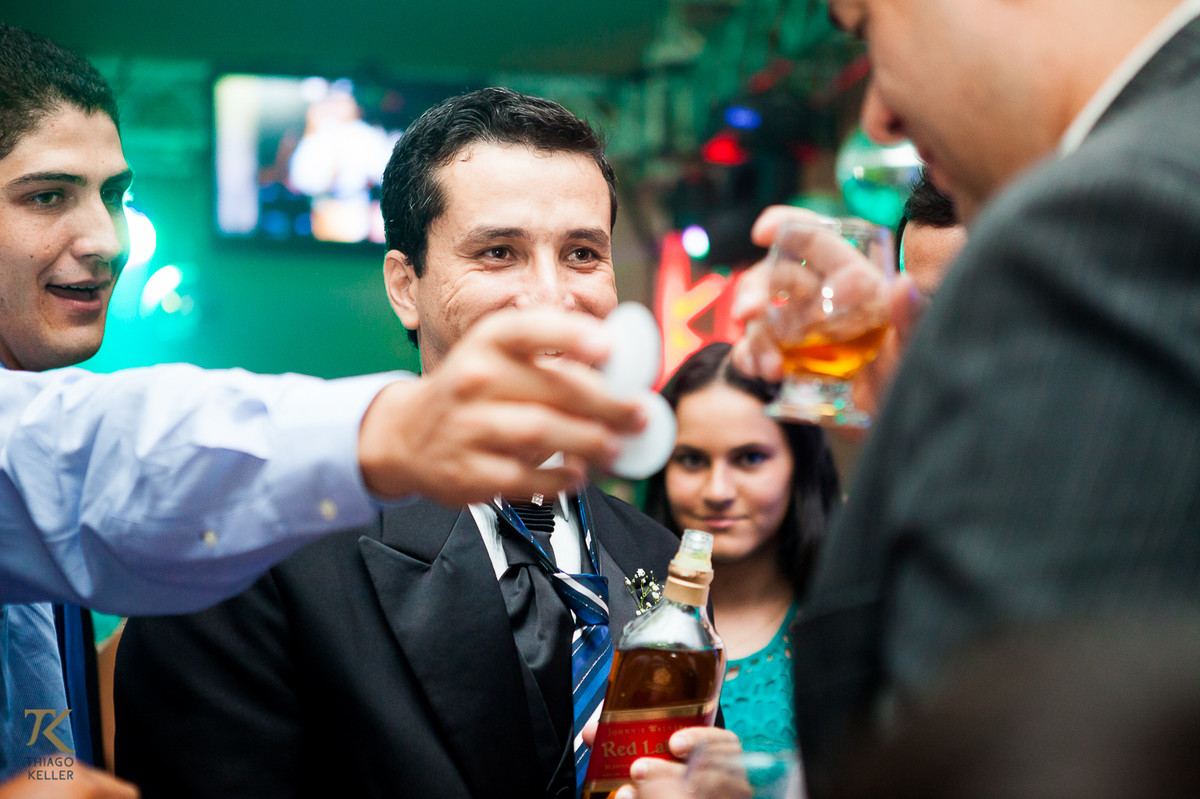 Fotografia de Casamento de Maura e Thiago realizado na cidade de Paracatu, Minas Gerais. Noivo bebe uísque durante a festa de casamento.