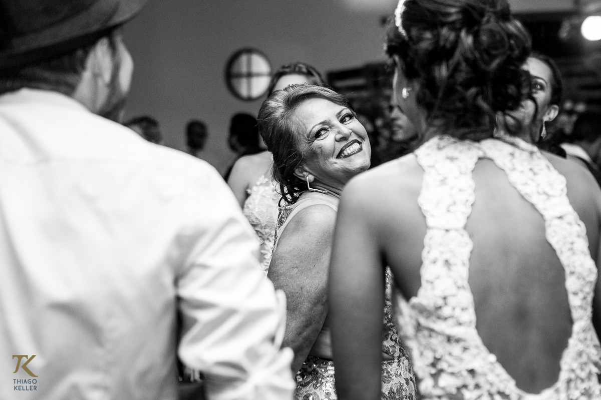 Fotografia de Casamento de Maura e Thiago realizado na cidade de Paracatu, Minas Gerais. Mãe da noiva sorri durante a festa de casamento.  Foto em preto e branco.