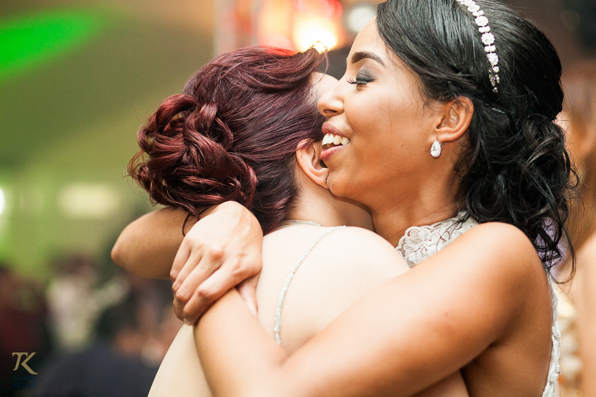 Fotografia de Casamento de Maura e Thiago realizado na cidade de Paracatu, Minas Gerais. Noiva é abraçada por amiga durante a festa.