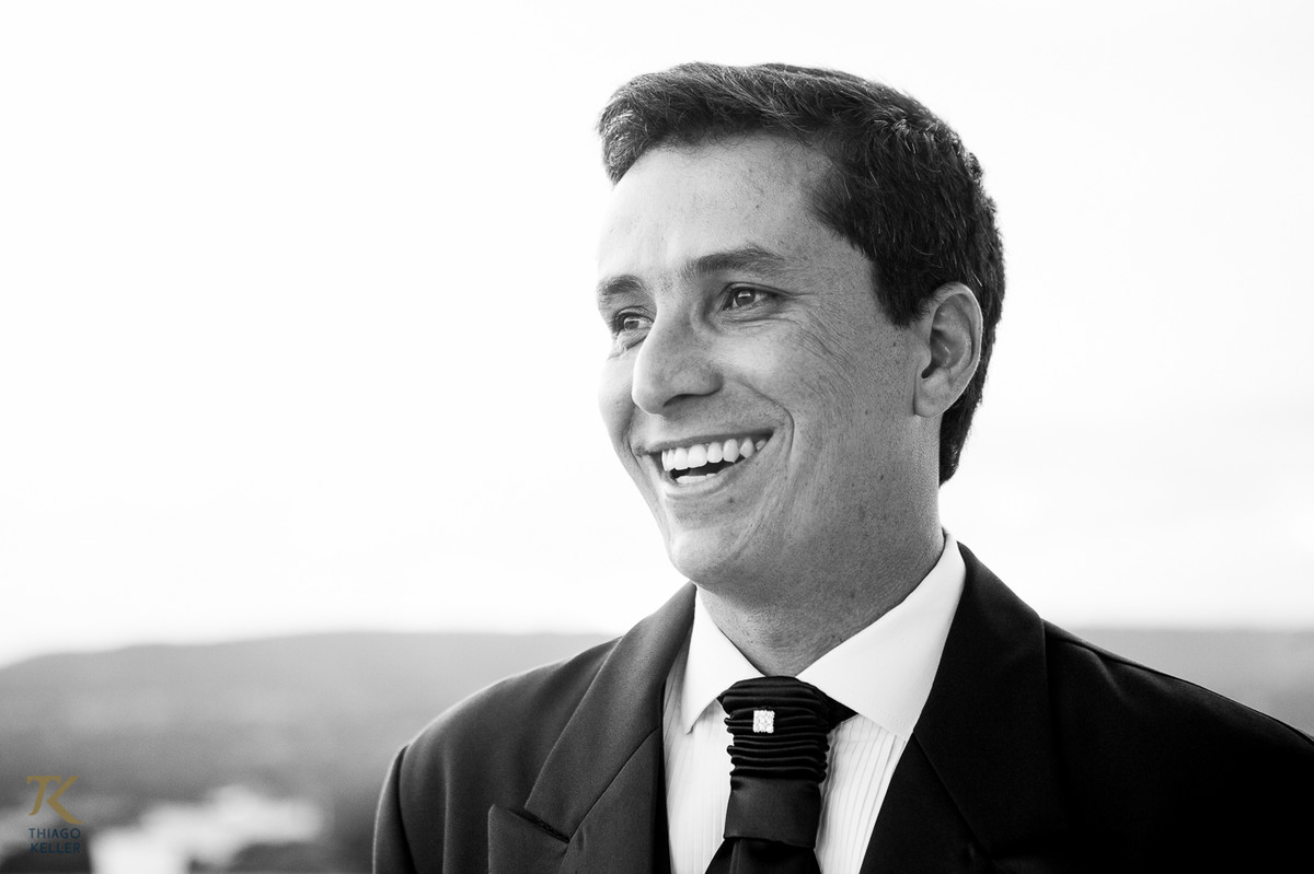 Fotografia de Casamento de Maura e Thiago realizado na cidade de Paracatu, Minas Gerais.  Noivo sorri durante making off. Foto em preto e branco.