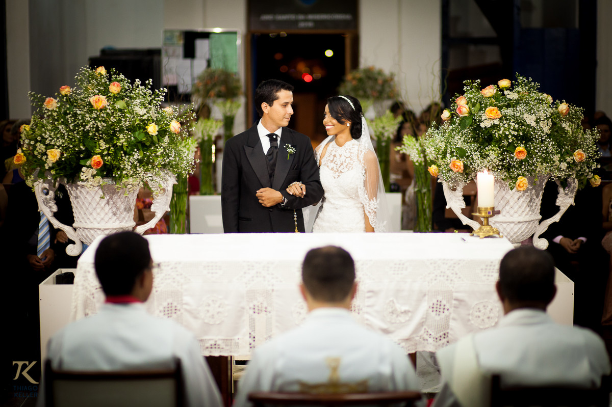 Fotografia de Casamento de Maura e Thiago realizado na cidade de Paracatu, Minas Gerais.  Casal sorri um para o outro no altar.