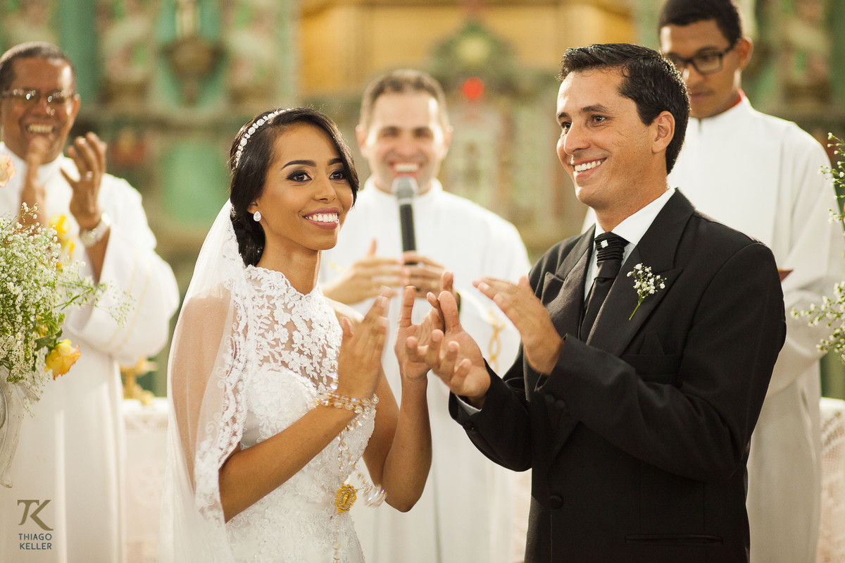 Fotografia de Casamento de Maura e Thiago realizado na cidade de Paracatu, Minas Gerais. Noivos batem palma ao fim da cerimônia.