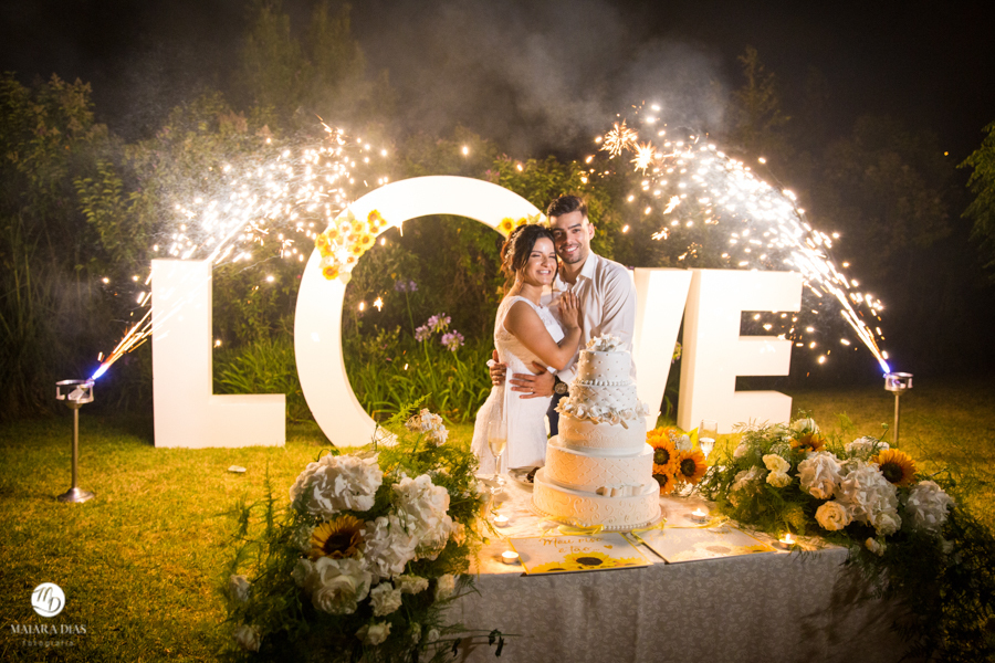 Casamento de dia Karine e Romulo na Quinta da Fonte do Paraiso na cidade de Lisboa - Portugal. Cerimonia ao ar livre na natureza e fotos feitas por Maiara Dias Fotografia. Corte do Bolo com o LOVE ao fundo. Fogos de artificio