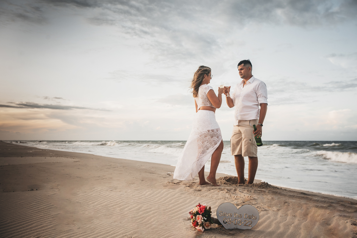 Noiva com vestido branco e  noivo de camisa branca com brinde na praia no pós wedding na praia do barro preto em Iguape