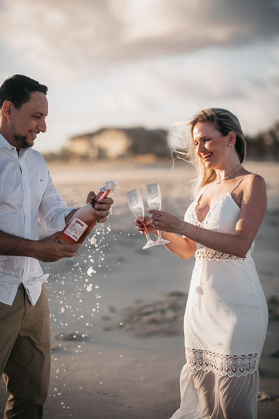 NOIVA COM VESTIDO BRANDO E NOIVO COM CAMISA BRANCA E CALÇA BEGE NUM ENSAIO PRE WEDDING NA SESSÃO EXTERNA NO POR DO SOL DA PRAIA DO BEACH PARK EM AQUIRAZ BRINDARAM A FELICIDADE DO CASAL JA PROXIMO DO SEU CASAMENTO