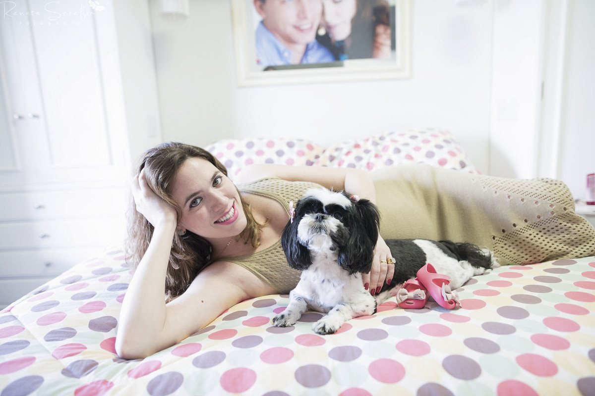 sessão de gestante feita pela fotógrafa de recem-nascido Renata Serafim mamae deitada na cama com o sapatinho do bebe e seu cachorrinho