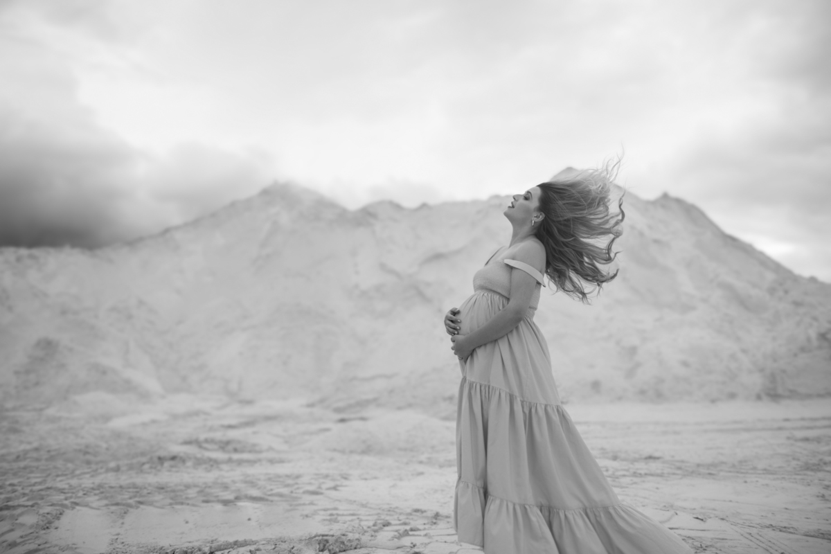 gestante, capturada enquanto o vento brinca com seu cabelo e vestido. O movimento do vento dá dinamismo à imagem, contrastando com a serenidade das dunas. Fotos feitas pelo fotógrafo de gestante Rafael Ohana em Brasília.