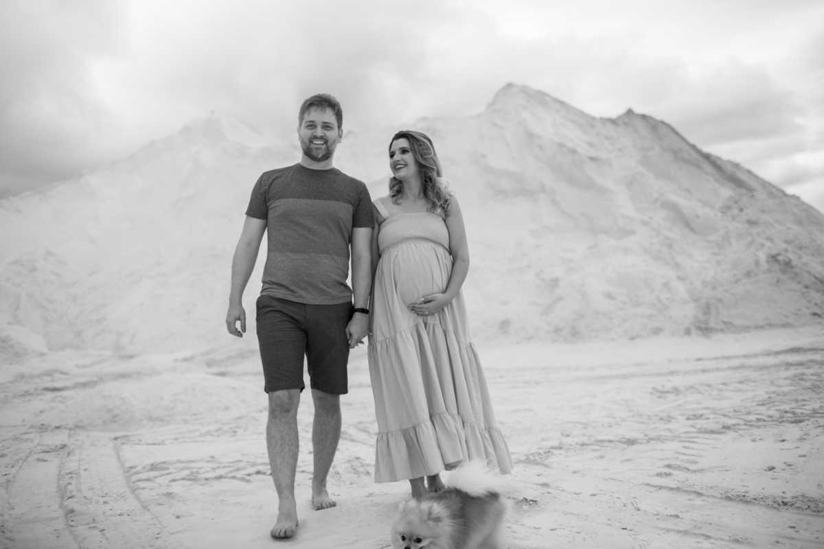 O casal caminhando nas dunas, lado a lado, com o cachorrinho acompanhando. A imagem evoca união, cumplicidade e a alegria de estarem juntos neste momento especial. Fotos feitas pelo fotógrafo de gestante Rafael Ohana em Brasília.