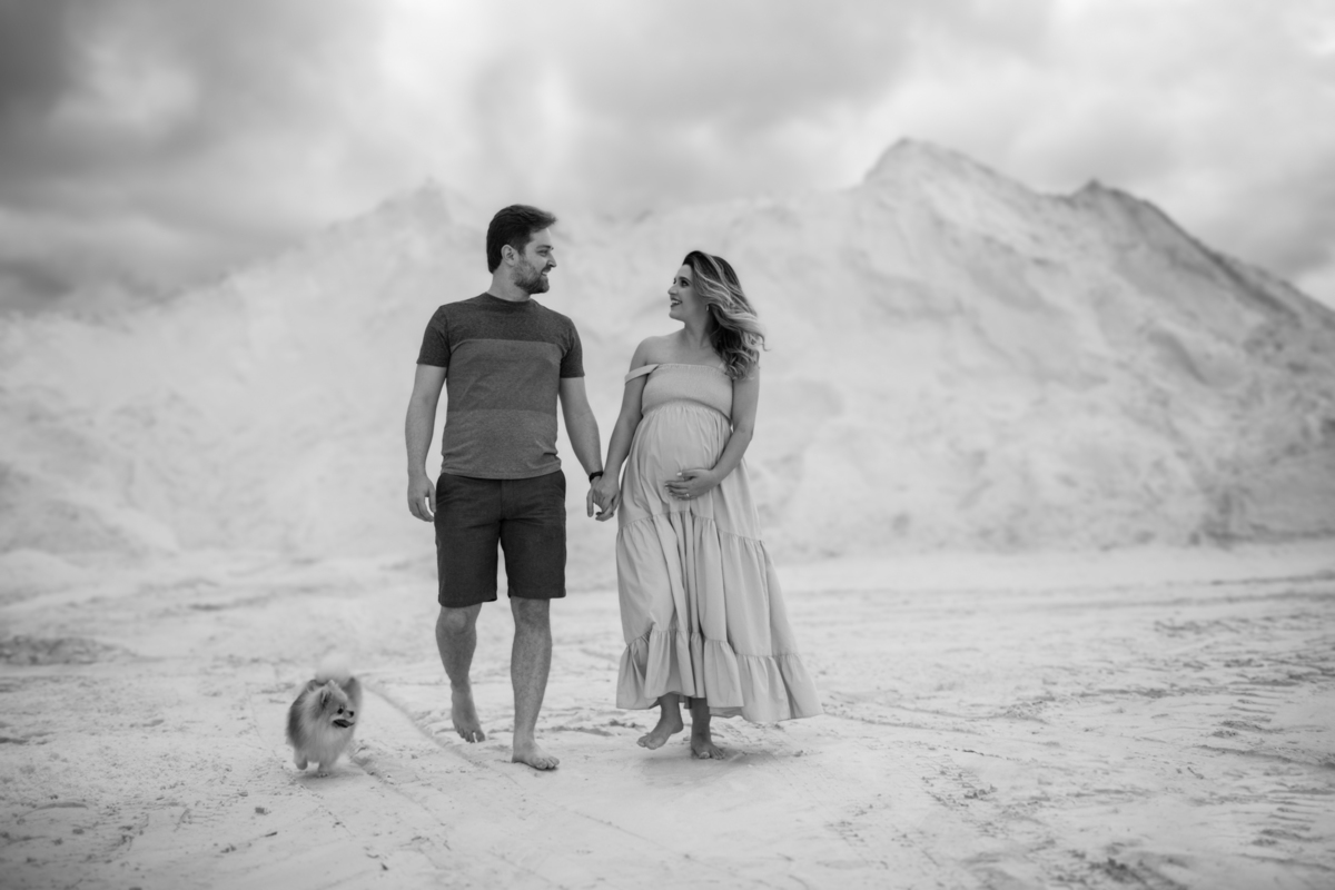 O casal caminhando nas dunas, lado a lado, com o cachorrinho acompanhando. A imagem evoca união, cumplicidade e a alegria de estarem juntos neste momento especial. Fotos feitas pelo fotógrafo de gestante Rafael Ohana em Brasília.
