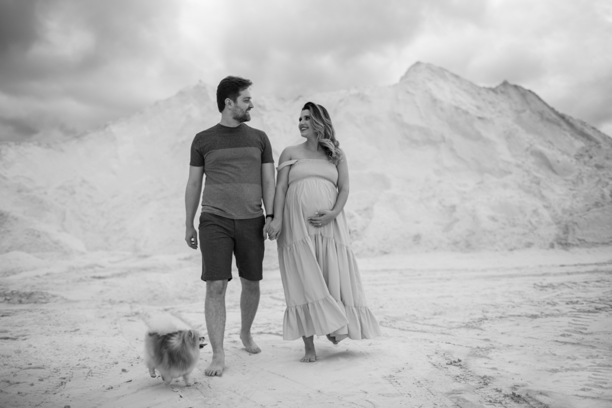 O casal caminhando nas dunas, lado a lado, com o cachorrinho acompanhando. A imagem evoca união, cumplicidade e a alegria de estarem juntos neste momento especial. Fotos feitas pelo fotógrafo de gestante Rafael Ohana em Brasília.