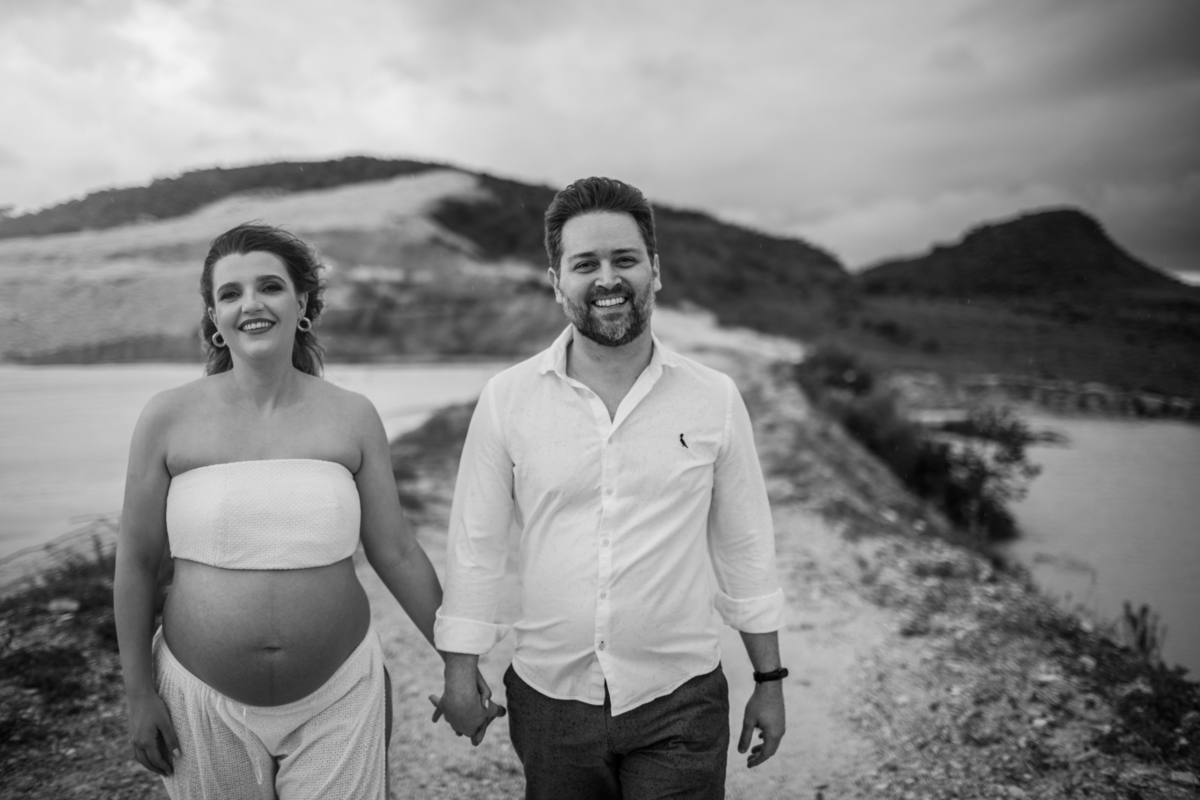 O casal andando de mãos dadas em um momento espontâneo e alegre, enquanto o vento sopra levemente o vestido da gestante, capturando a leveza e a conexão entre os dois. Fotos feitas pelo fotógrafo de gestante Rafael Ohana em Brasília.