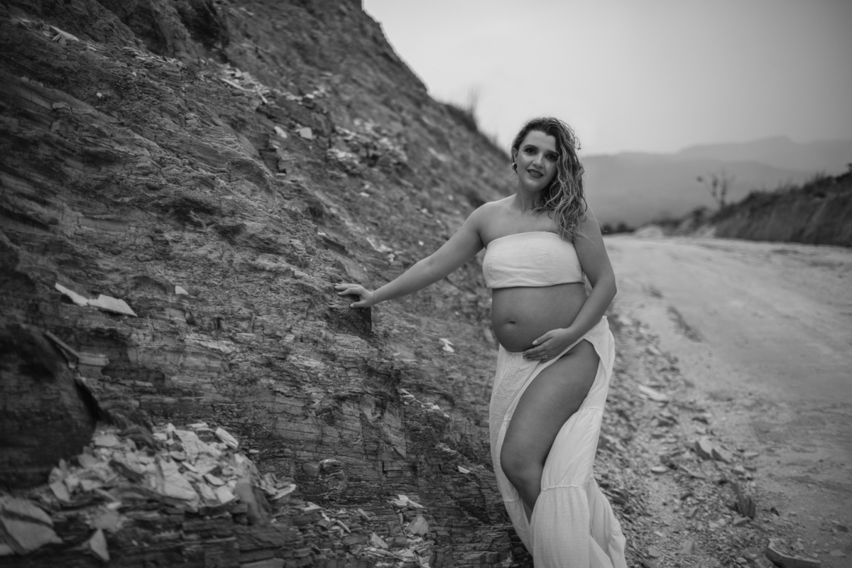 A gestante caminhando ao longo de uma colina, com a mão sobre a barriga, enquanto o cenário montanhoso ao fundo adiciona um toque de aventura à imagem. Fotos feitas pelo fotógrafo de gestante Rafael Ohana em Brasília.