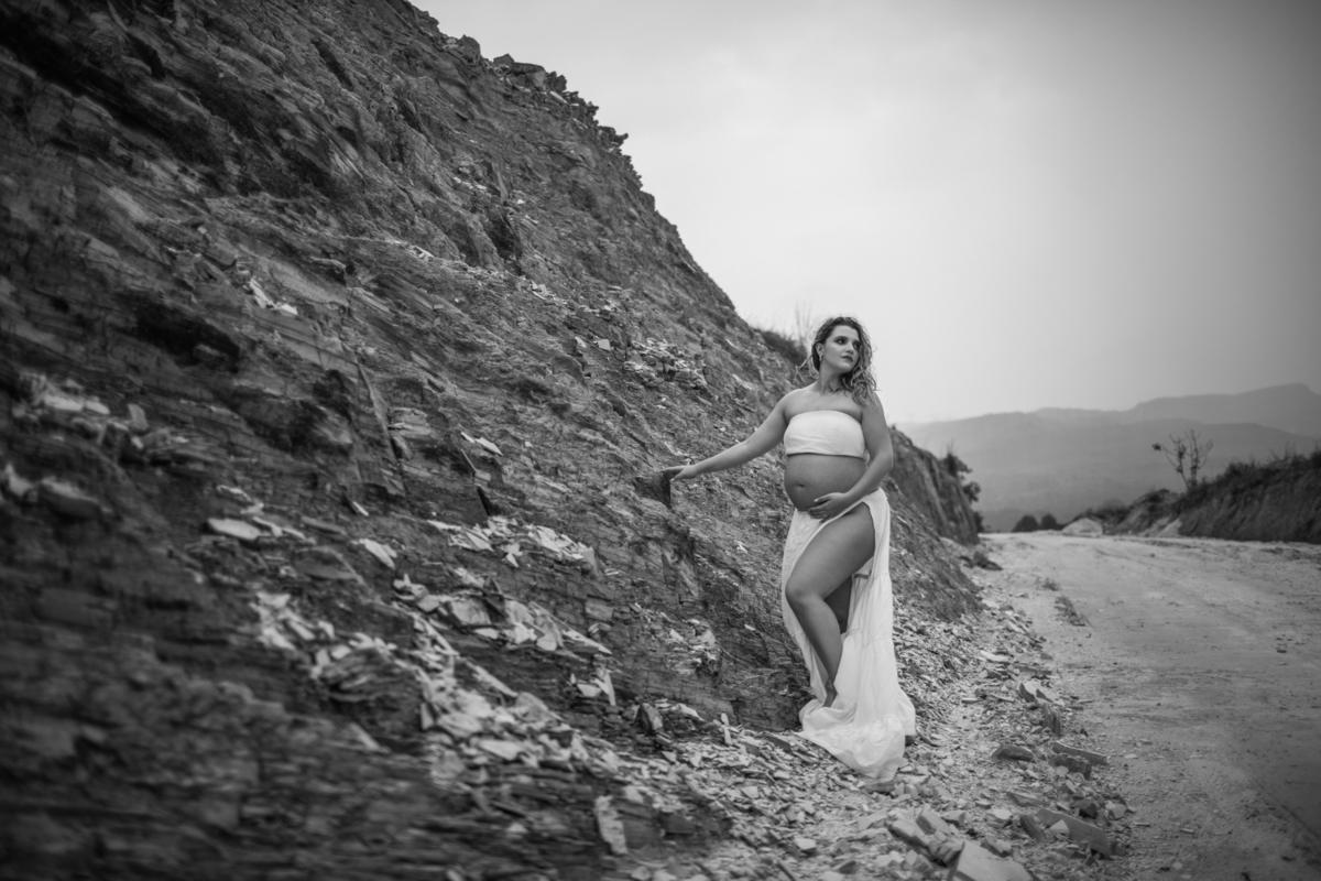 A gestante caminhando ao longo de uma colina, com a mão sobre a barriga, enquanto o cenário montanhoso ao fundo adiciona um toque de aventura à imagem. Fotos feitas pelo fotógrafo de gestante Rafael Ohana em Brasília.