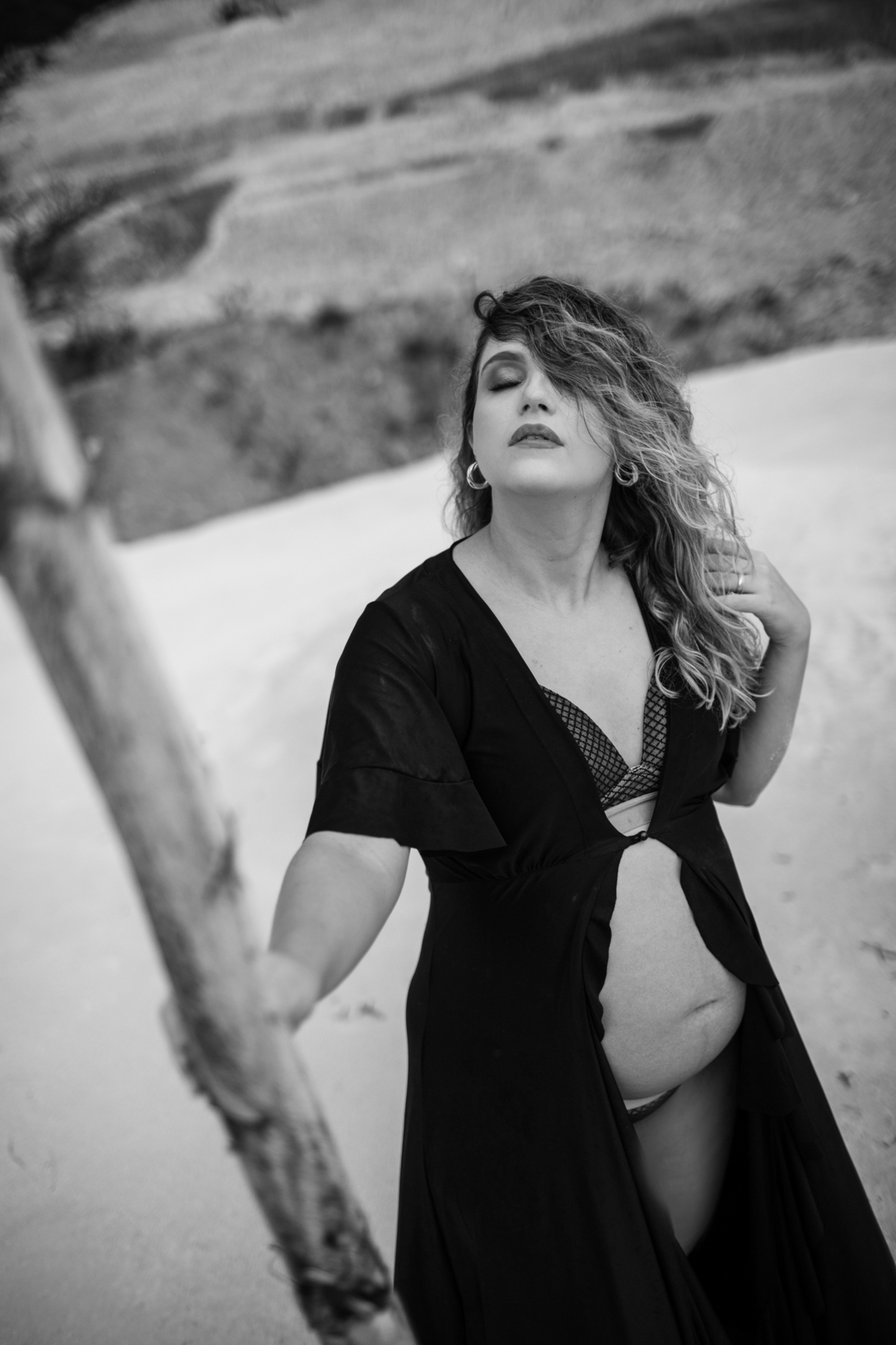 Close-up da gestante em pé, com a mão sobre a barriga e o cabelo ao vento. A expressão contemplativa dela e o ambiente natural ao redor trazem uma sensação de paz e força. Fotos feitas pelo fotógrafo de gestante Rafael Ohana em Brasília.