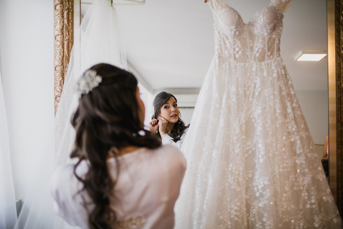 noiva colocando brincos na frente do espelho Crédito: Fotógrafo de casamento Rafael Ohana feito em Brasília-DF