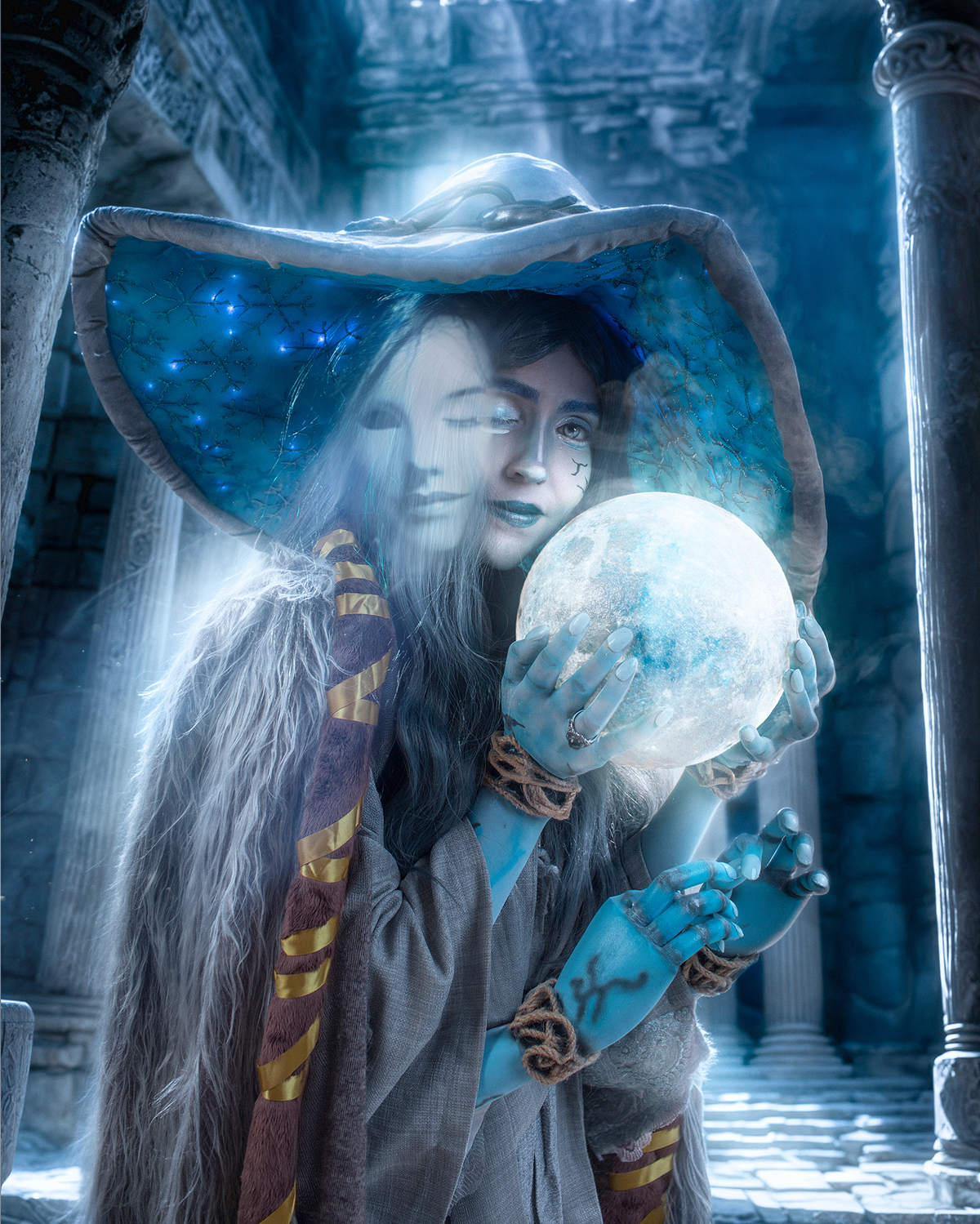 Cosplay de Ranni (Elden Ring). Mulher azul com chapéu mágico segura uma esfera brilhante em cenário de ruínas misteriosas, com espírito translúcido ao lado. Atmosfera mística e épica. Foto por Rafael Ohana em Brasília.