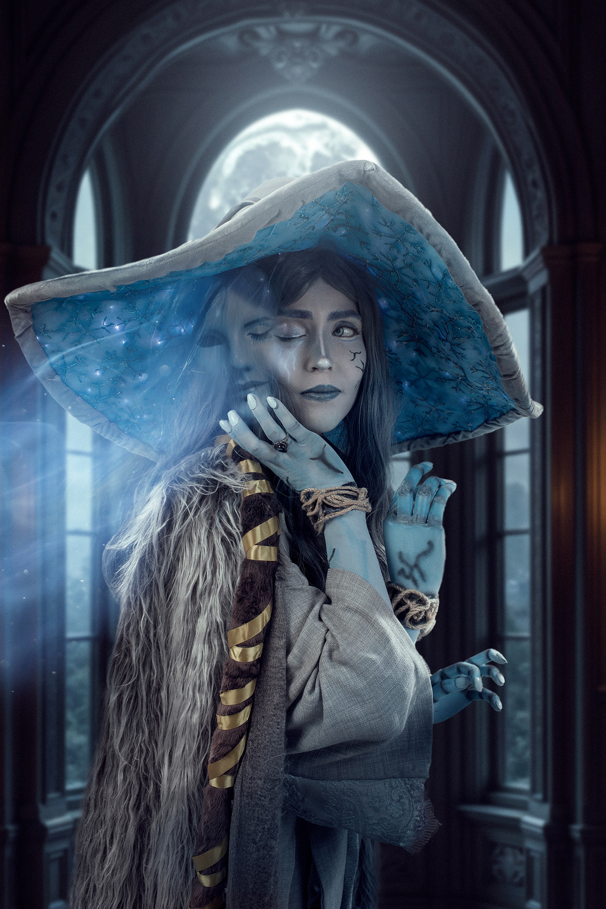 Cosplay de Ranni (Elden Ring). Figura feminina em close-up, com chapéu estrelado e pele azul, destacando espírito translúcido e atmosfera mágica em castelo. Foto por Rafael Ohana em Brasília.
