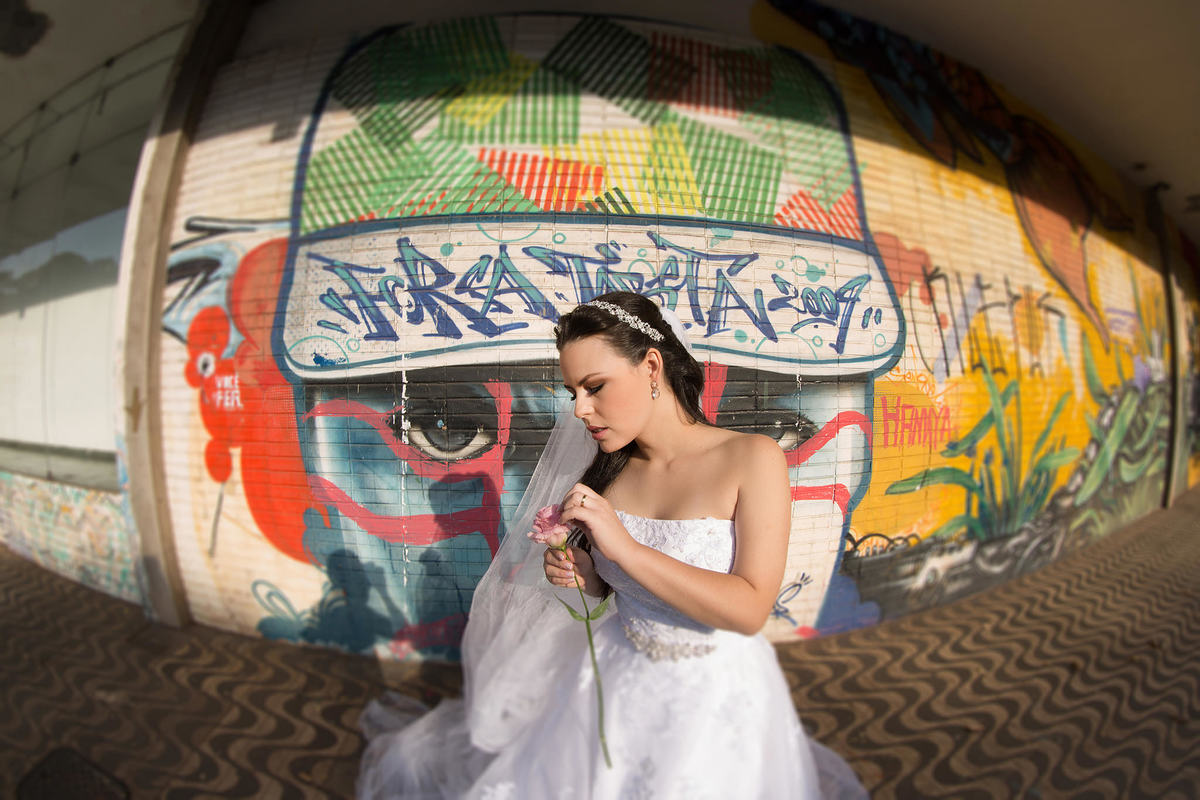 Noiva mexendo em petalas de flores em frente a uma parede grafitada