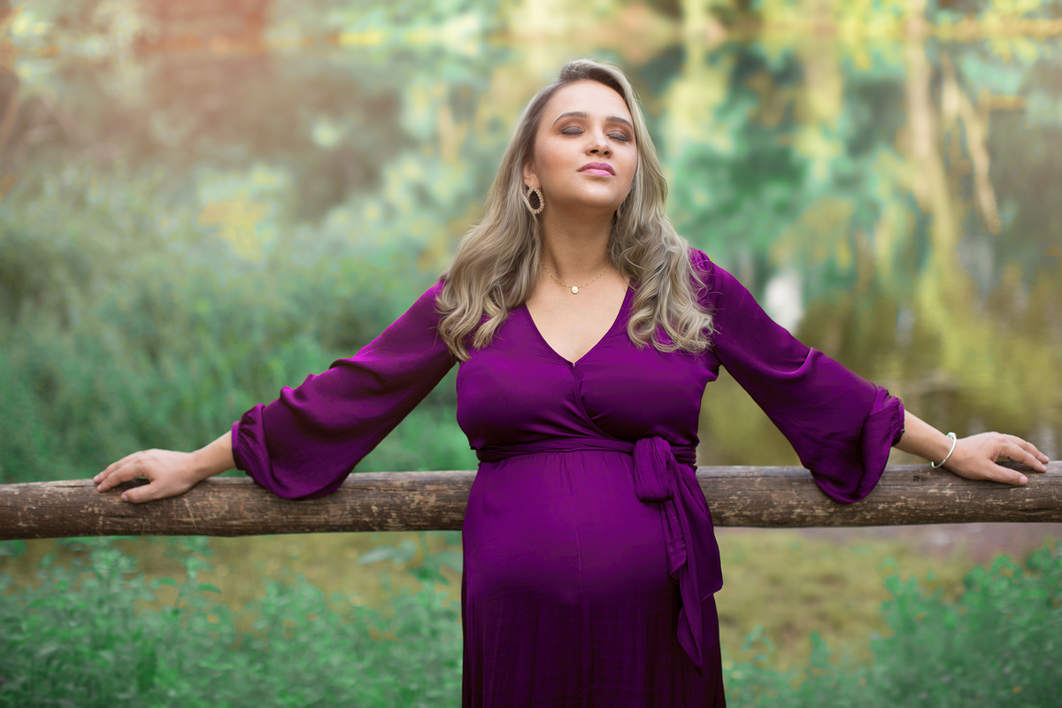 Grávida encostada em cerca de madeira no parque olhos dagua com lagoa ao fundo. Fotofeita pelo fotógrafo Rafael Ohana fotógrafo de gestante em brasília.