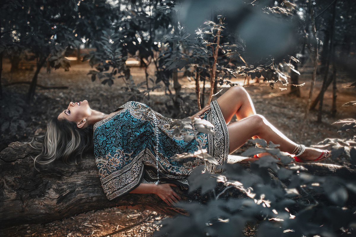 Mulher deitada em tronco de àrvore em bosque. 