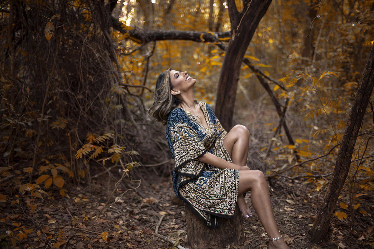 Mulher sentada na floresta sorrindo para o alto. Ensaio feminino feito pelo fotógrafo Rafael Ohana no Parque Olhos D´água em Brasília-DF 