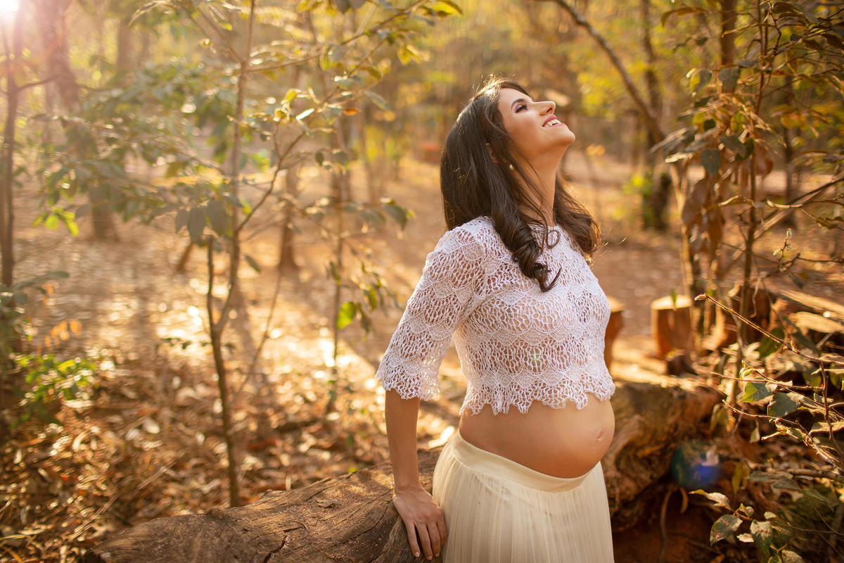 Grávida sorrindo encostada em árvore. Foto feita pelo fotógrafo Rafael Ohana no parque Olhos D´água em Brasília-DF.