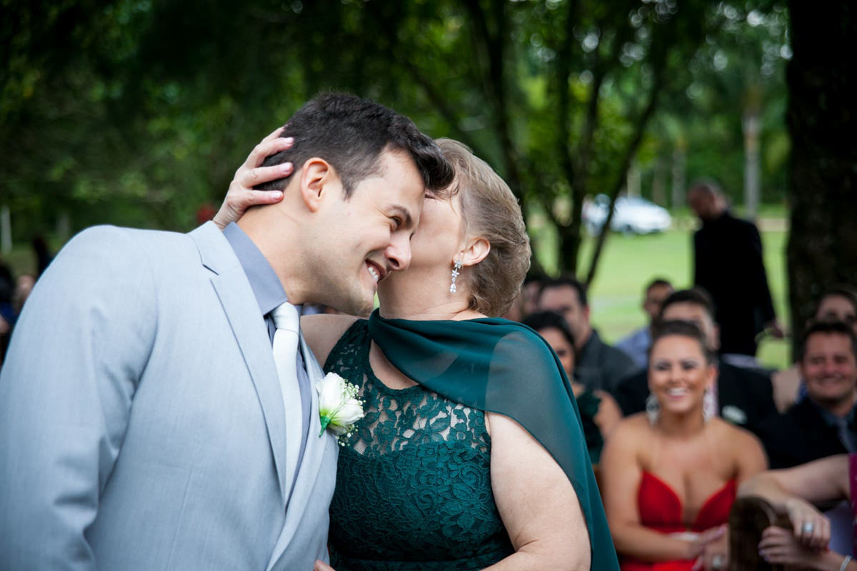 Casamento ao ar livre e de dia dos noivos Anny e Rodolfo fotografado pelo melhor fotógrafo de Campo Largo e região de Curitiba, Michel Druziki. Mãe do noivo beijando o noivo no altar