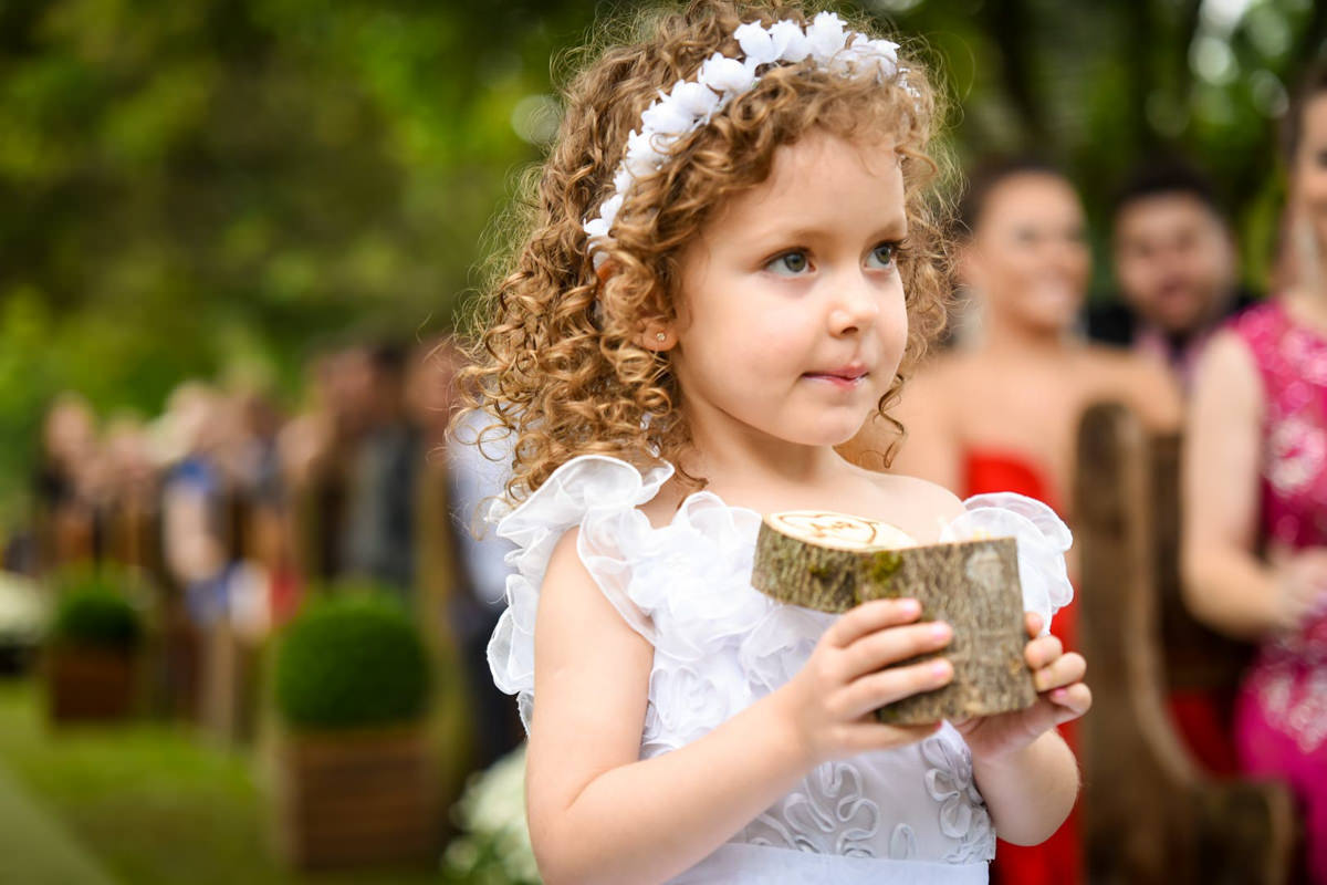 Casamento ao ar livre e de dia dos noivos Anny e Rodolfo fotografado pelo melhor fotógrafo de Campo Largo e região de Curitiba, Michel Druziki. Daminha com as alianças no troco de madeira