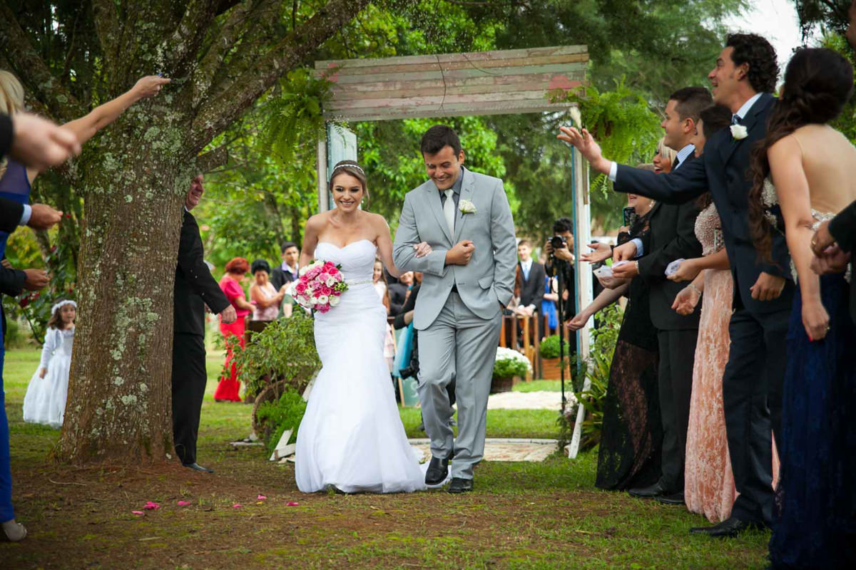 Casamento ao ar livre e de dia dos noivos Anny e Rodolfo fotografado pelo melhor fotógrafo de Campo Largo e região de Curitiba, Michel Druziki. Noivos saindo da cerimônia sorrindo e com chuva de arroz