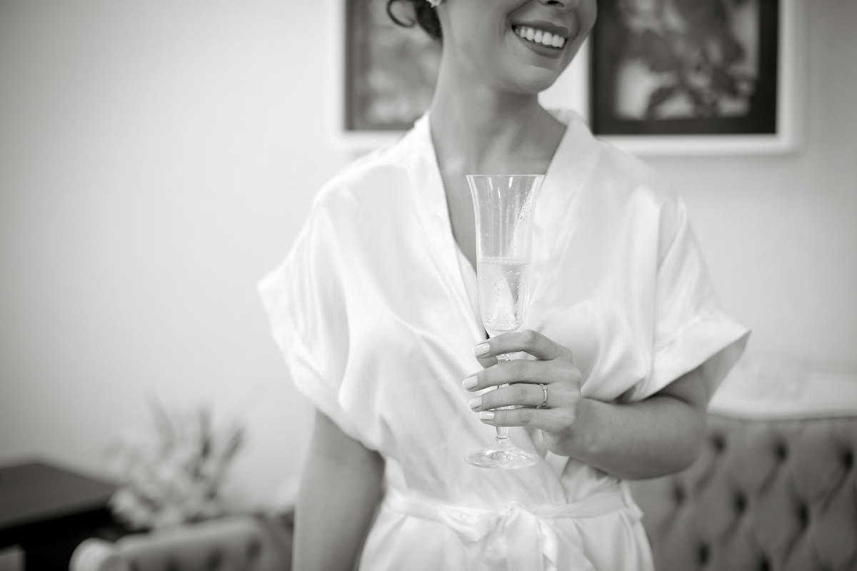 O fotógrafo de casamentos Michel Druziki em Campo Largo e Curitiba, fotografou making of da noiva Camila, no salão Camaleão Cabelo e Estética. Noiva sorrindo com uma taça de champagne 