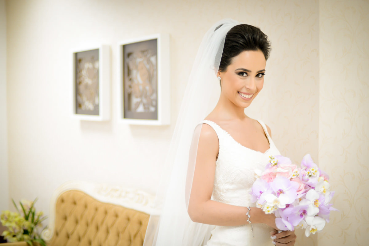 O fotógrafo de casamentos Michel Druziki em Campo Largo e Curitiba, fotografou making of da noiva Camila, no salão Camaleão Cabelo e Estética. Noiva sorrindo com buquê de orquídeas lilás
