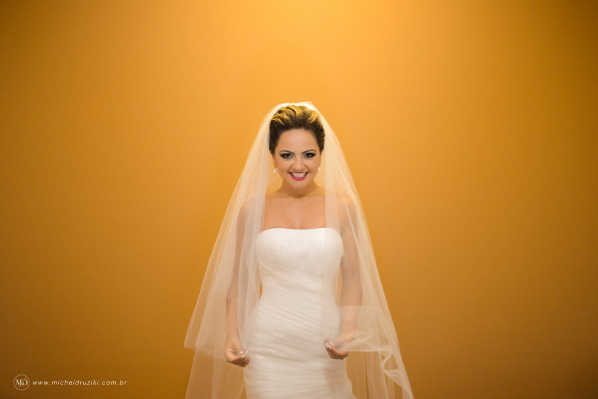 Casamento na praia do casal Dani e André fotografado pelo melhor fotógrafo de casamentos e ensaios de campo largo e Curitiba, Michel Druziki. Noiva em frente a uma parede amarela, segurando o véu e sorrindo