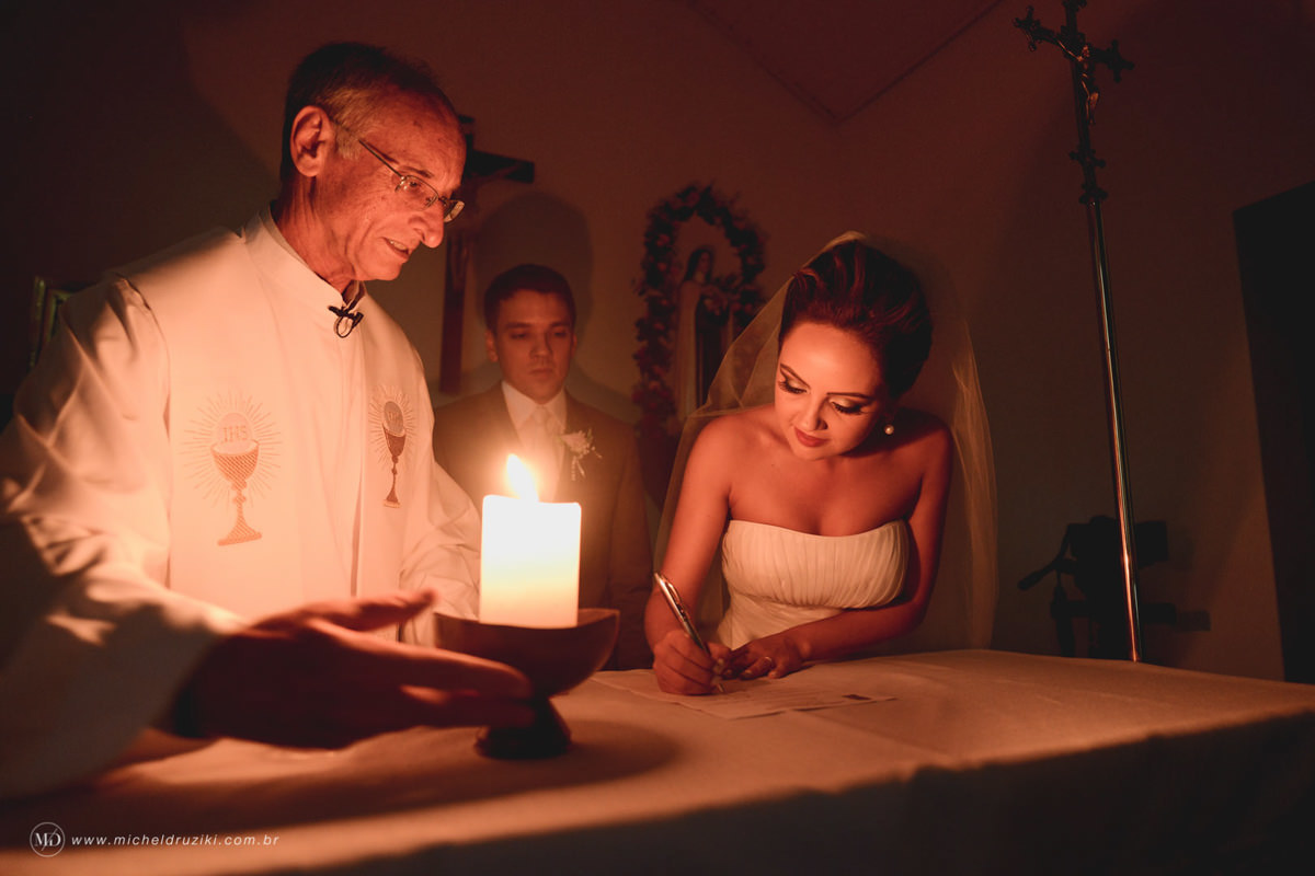 Casamento na praia do casal Dani e André fotografado pelo melhor fotógrafo de casamentos e ensaios de campo largo e Curitiba, Michel Druziki. Noiva assinando o termo de casamento à luz de velas