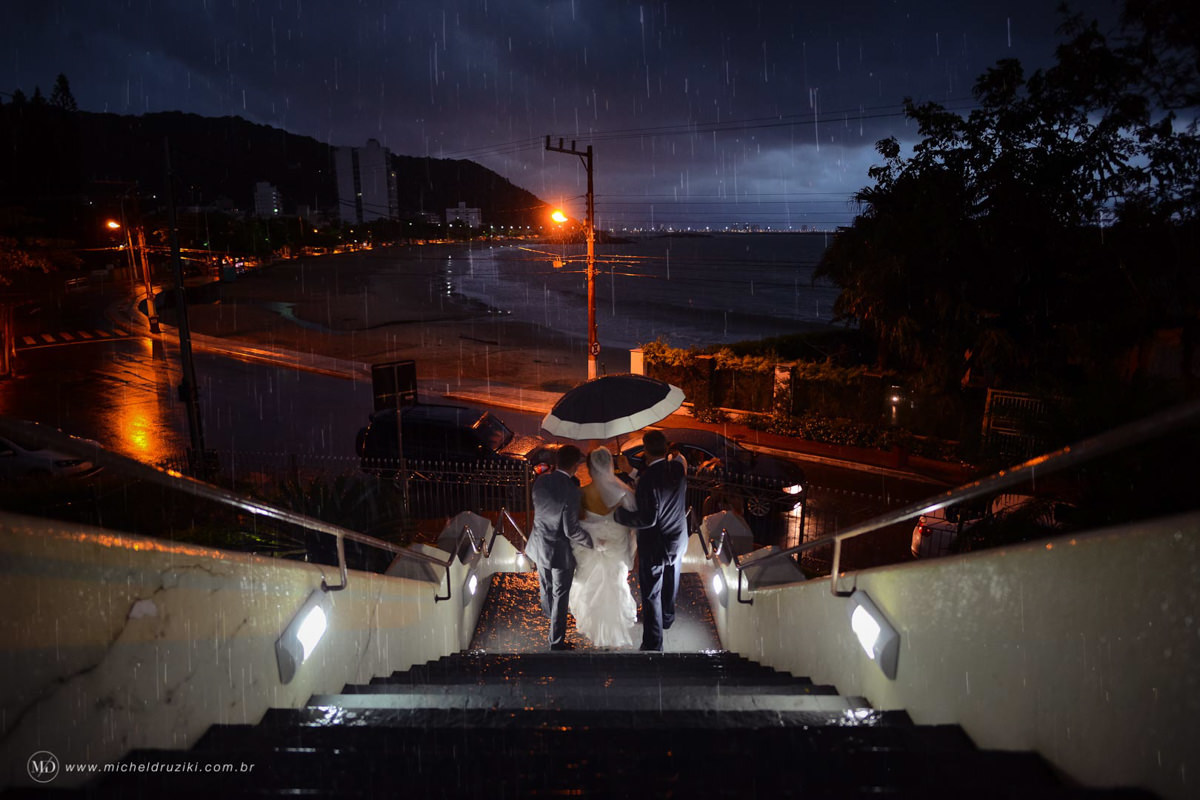 Casamento na praia do casal Dani e André fotografado pelo melhor fotógrafo de casamentos e ensaios de campo largo e Curitiba, Michel Druziki. Noiva sendo levada com guarda chuva em frente ao mar