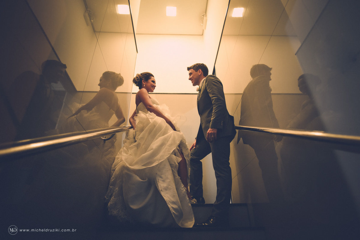 Casamento na praia do casal Dani e André fotografado pelo melhor fotógrafo de casamentos e ensaios de campo largo e Curitiba, Michel Druziki. Noivos encostados nas paredes espelhadas na escada