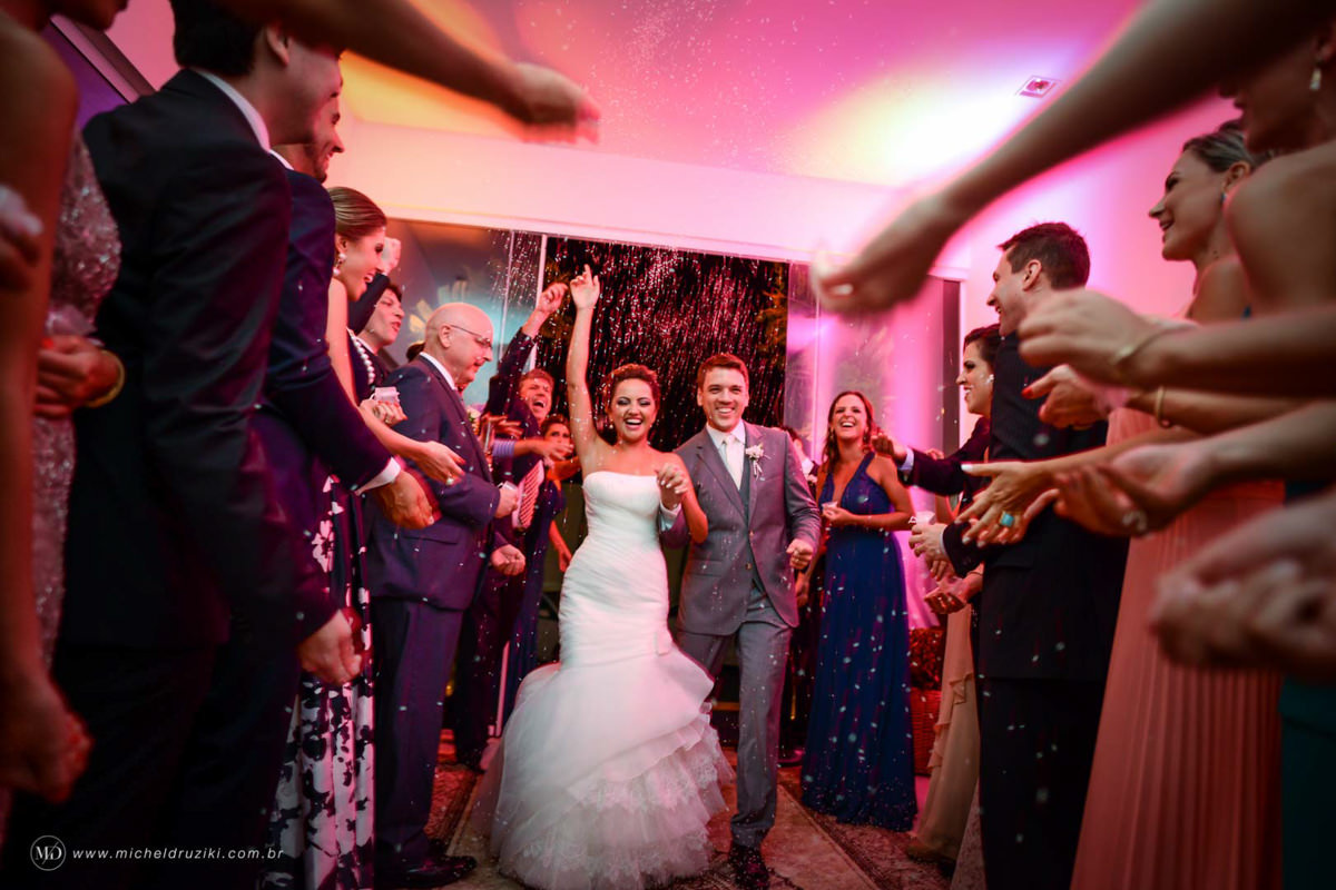 Casamento na praia do casal Dani e André fotografado pelo melhor fotógrafo de casamentos e ensaios de campo largo e Curitiba, Michel Druziki. Noivos entrando no salão de festas com chuva de arroz