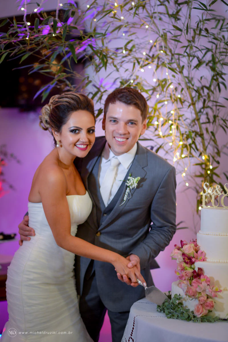 Casamento na praia do casal Dani e André fotografado pelo melhor fotógrafo de casamentos e ensaios de campo largo e Curitiba, Michel Druziki. Noivos cortando o bolo no cenário rosa