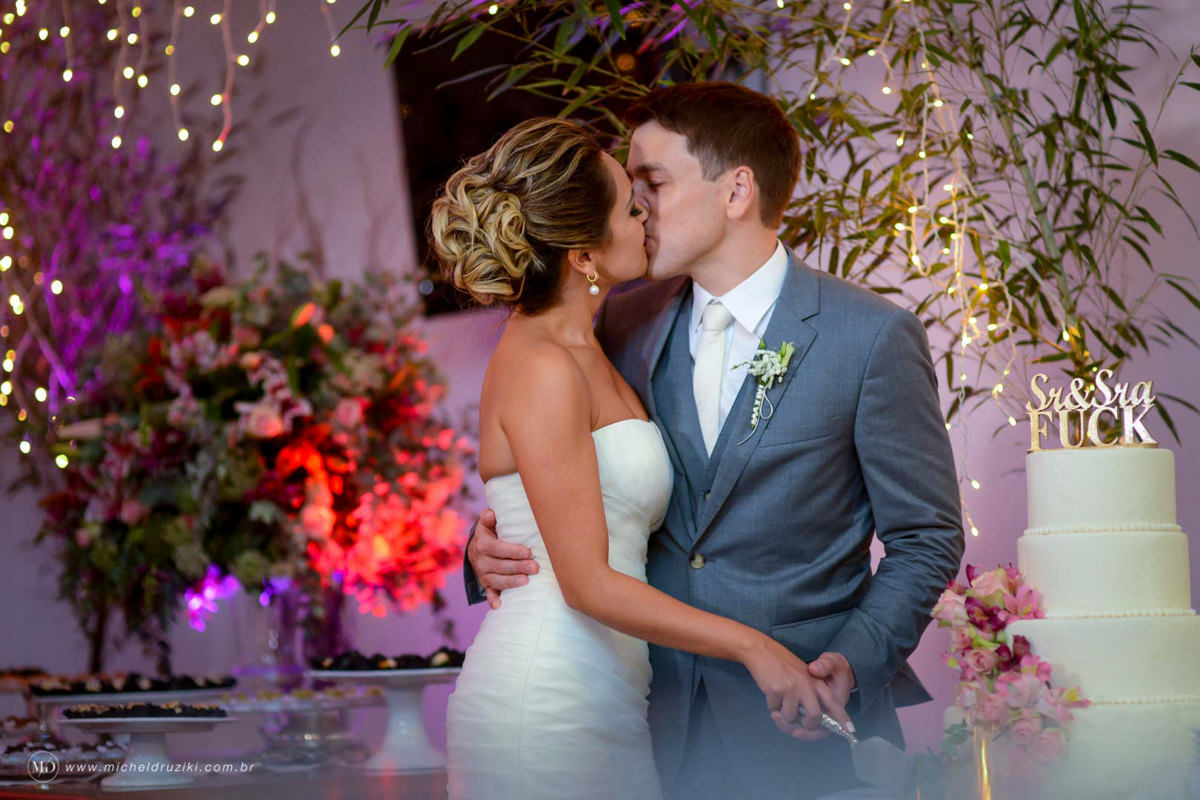 Casamento na praia do casal Dani e André fotografado pelo melhor fotógrafo de casamentos e ensaios de campo largo e Curitiba, Michel Druziki. Noivos cortando o bolo e se beijando