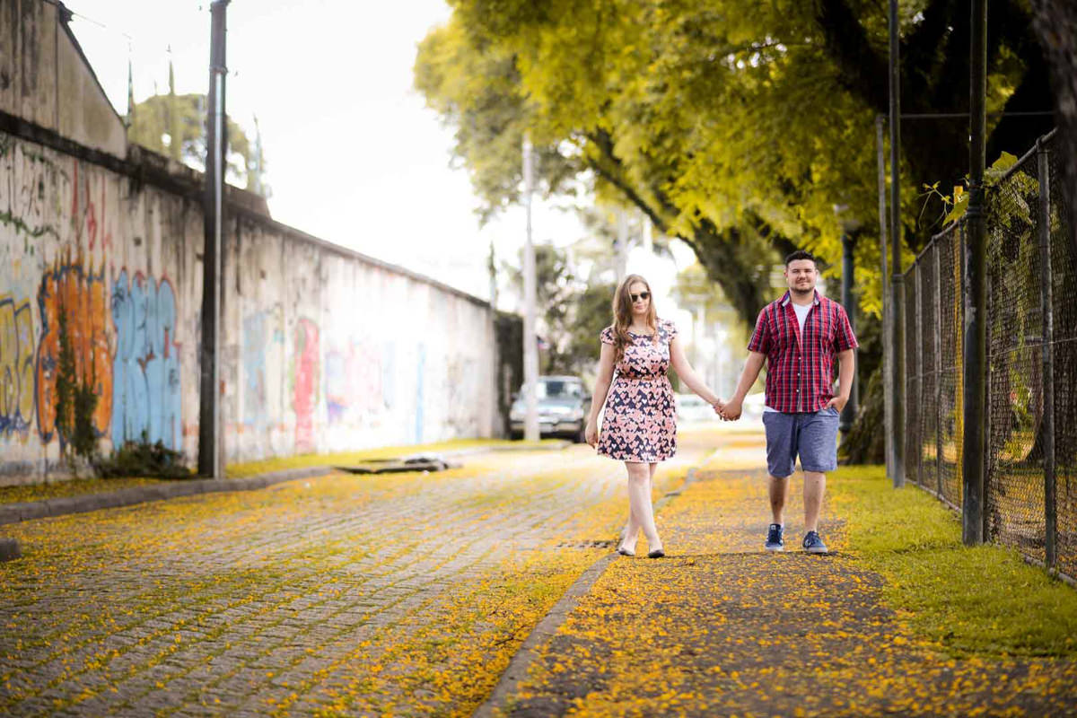 Ensaio pre wedding do casal Kelly e Flávio fotografado pelo melhor fotógrafo de ensaios e casamento em Campo Largo e Curitiba, Michel Druziki. Noivos de mãos dadas andando pela rua florida