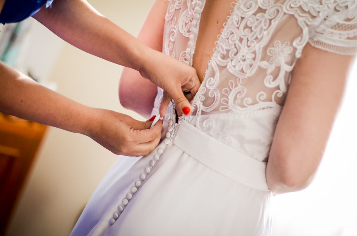 Casamento ao ar livre e de dia dos noivos Kelly e Flávio fotografado pelo melhor fotógrafo de Campo Largo e região de Curitiba, Michel Druziki. Fechando o vestido da noiva de renda 