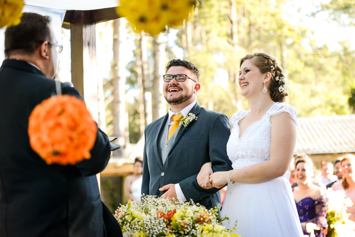 Casamento ao ar livre e de dia dos noivos Kelly e Flávio fotografado pelo melhor fotógrafo de Campo Largo e região de Curitiba, Michel Druziki. Noivos sorrindo durante a cerimônia 