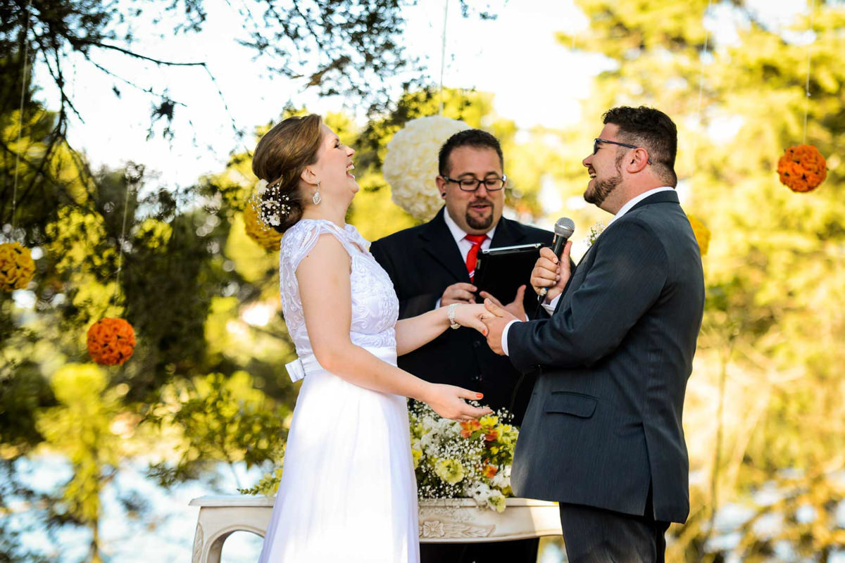 Casamento ao ar livre e de dia dos noivos Kelly e Flávio fotografado pelo melhor fotógrafo de Campo Largo e região de Curitiba, Michel Druziki. Noivos dando risada no altar trocando as alianças
