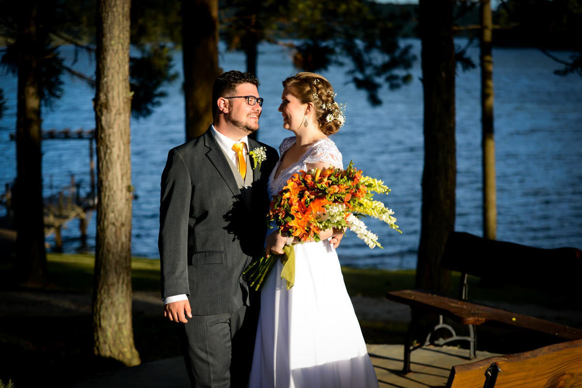 Casamento ao ar livre e de dia dos noivos Kelly e Flávio fotografado pelo melhor fotógrafo de Campo Largo e região de Curitiba, Michel Druziki. Noivos abraçados e sorrindo em frente ao lago