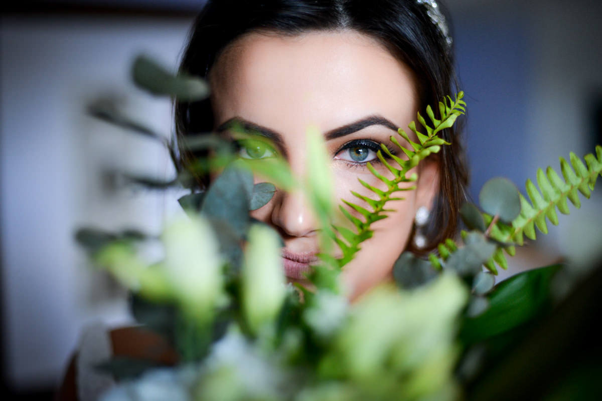 Casamento dos noivos Neriane e Eduardo fotografado pelo melhor fotógrafo de casamentos e ensaios de campo largo e Curitiba, Michel Druziki. Olhos azuis da noiva em meio as folhas verdes do buquê