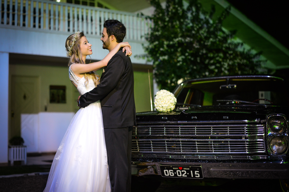 Casamento dos noivos Roxanne e Diego fotografado pelo melhor fotógrafo de Campo Largo e região de Curitiba, Michel Druziki. Noivos encostados no carro abraçados em frente à casa