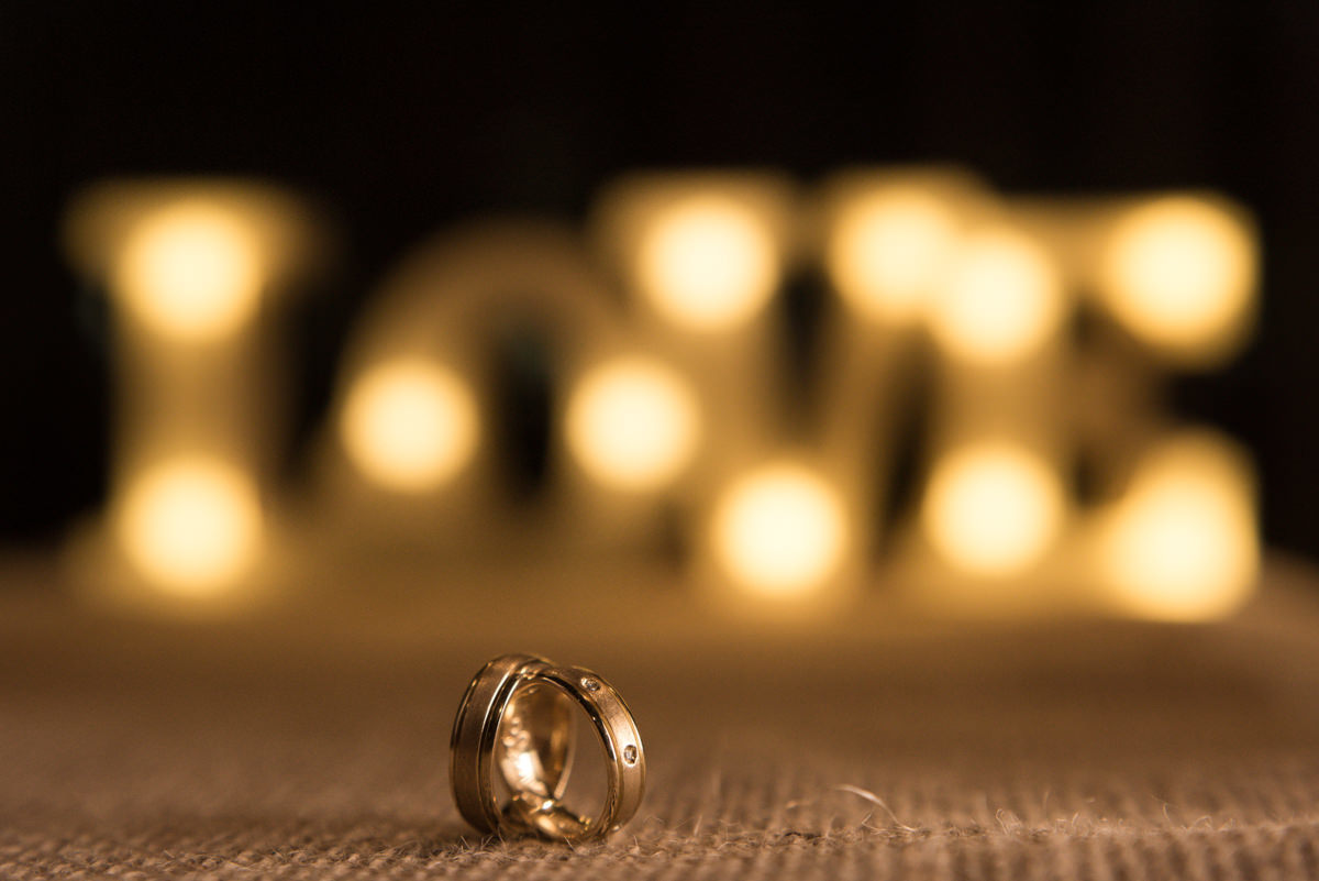 Casamento dos noivos Ana Paula e Saulo, fotografado pelo melhor fotógrafo de ensaios e casamento em Campo Largo e Curitiba, Michel Druziki. Alianças de casamento em foco e luminária love desfocada