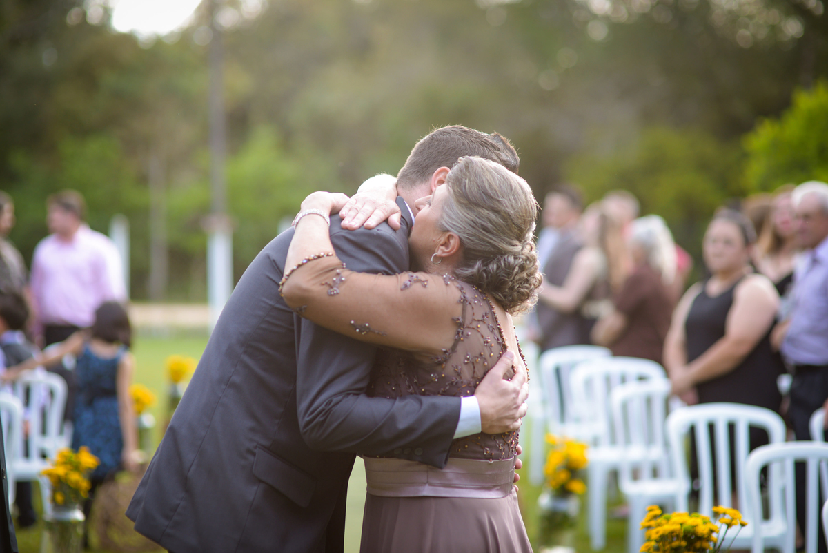 Casamento de dia ao ar livre dos noivos Cheila e Lúcio, no Negrão Eventos, fotografado pelo melhor fotógrafo de casamentos de campo largo e Curitiba, Michel Druziki. Mãe do noivo abraçando o noivo no altar