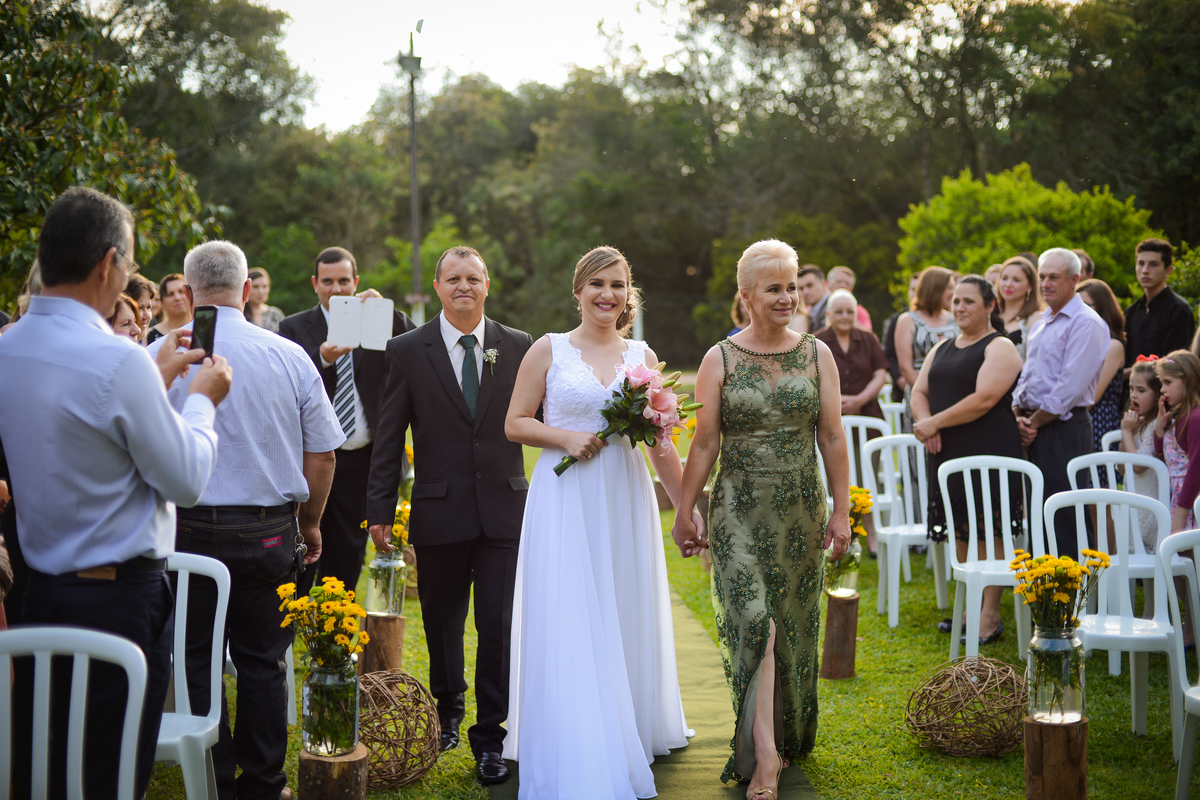 Casamento de dia ao ar livre dos noivos Cheila e Lúcio, no Negrão Eventos, fotografado pelo melhor fotógrafo de casamentos de campo largo e Curitiba, Michel Druziki. Noiva entrando acompanhada dos pais